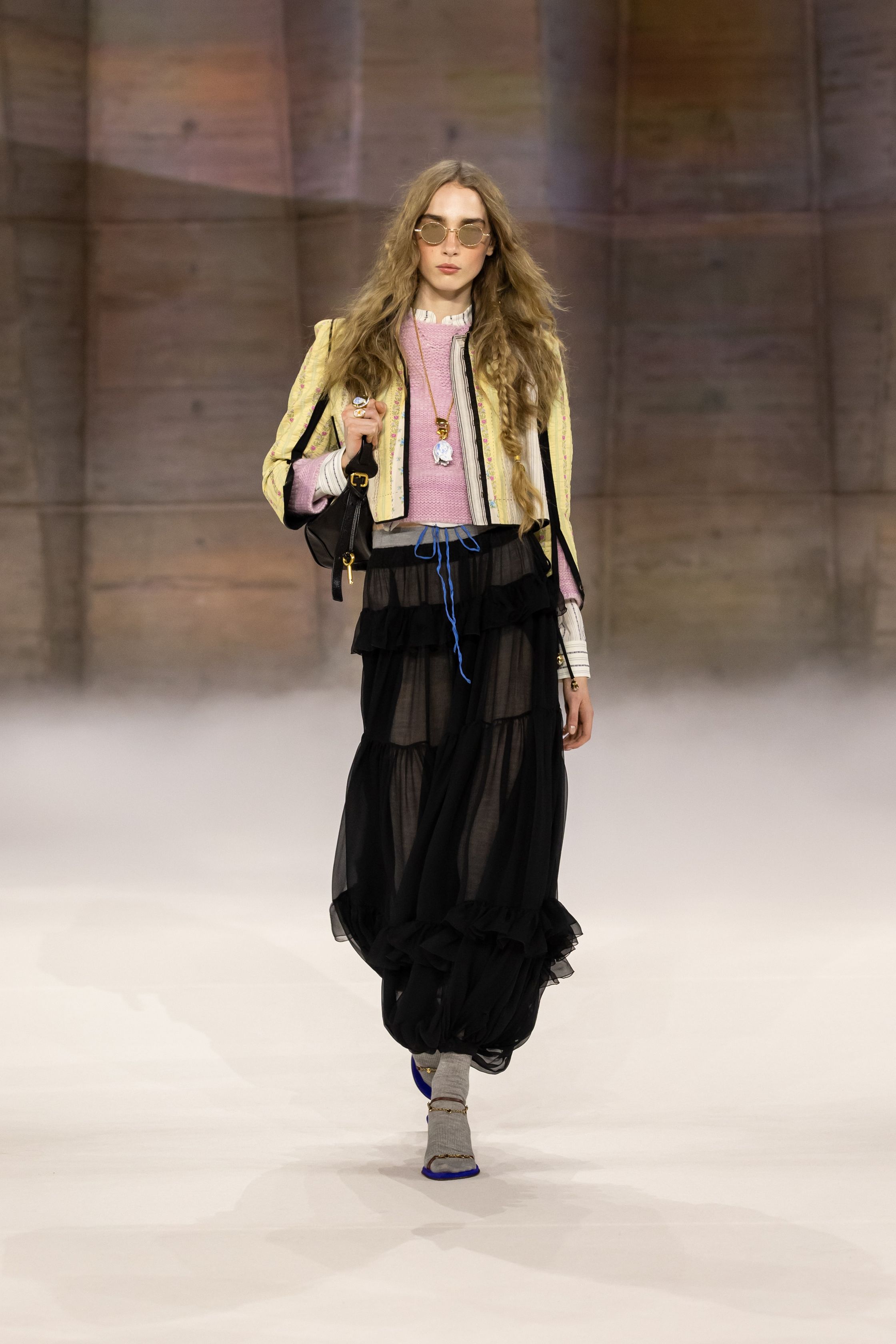 Chloé在2026秋冬继续书写品牌标志性的波西米亚浪漫，通过流动长裙、皮革长靴与柔软披风构建自由而诗意的女性形象。系列色调以大地色、酒红与米色为主，搭配轻盈薄纱与羊毛外套，使整体造型既温暖又富有层次。民族图案、长流苏与复古轮廓让整个系列充满旅行与冒险气息，呈现出典型的Chloé式自由精神-顽石频道趋势研究